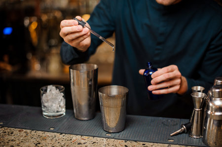 Barman adding some blue dye into a shaker making summer cocktail on the bar counter