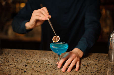 Barman decorating a fresh and sweet blue cocktail with a little slice of orange on the bar counterの写真素材