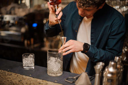 Bartender adding an alcoholic drink into a measuring cup on the bar counter on the blurred backgroundの写真素材
