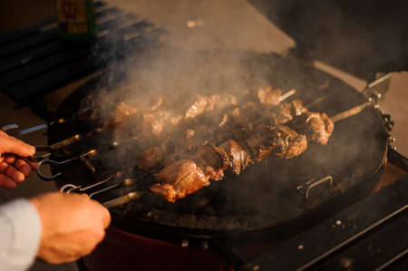 Man roasting a large meat pieces on the skewer on the grill. Cooking a very delicious shashlikの写真素材