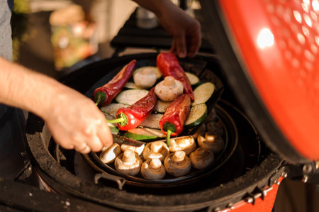 Man placed a plate with big red peppers, mushrooms and sliced egg-plants to the grill