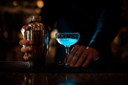 Man hands holding a glass with blue summer cocktail and little bottle on the bar counterの写真素材