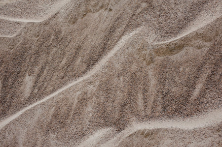 Wet brown sand texture . Background of wet sand lying like waves because of the wind on the coast