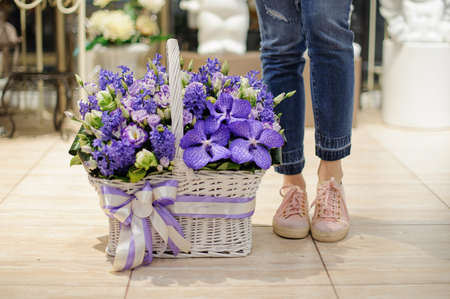 Girl standing near to a beautiful basket consisting of spring violet flowers decorated with a bowの写真素材