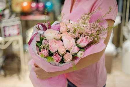 Florist holding a tender pink flower composition consisting of ranunculus, peonies and other beautiful flowers in a flower shopの写真素材