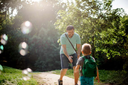 Happy father walking in the summer park and playing with soap bubbles with his little sonの写真素材