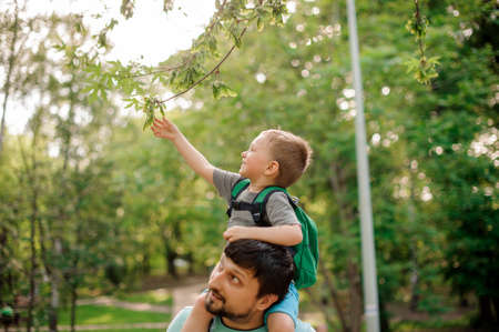 Bearded father carrying his little son on his shoulders walking in the green summer parkの写真素材