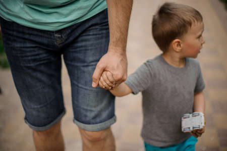 Father hand holding a little hand of his son walking down the street on warm dayの写真素材