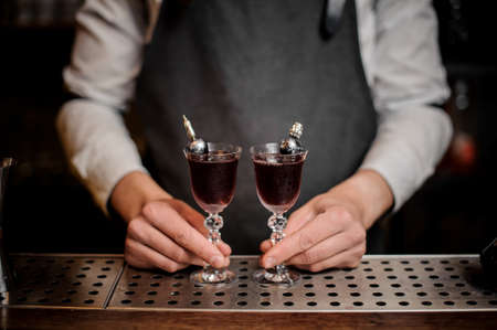 Bartender holding two elegant glasses filled with sweet summer Arnaud cocktail on the bar counterの写真素材