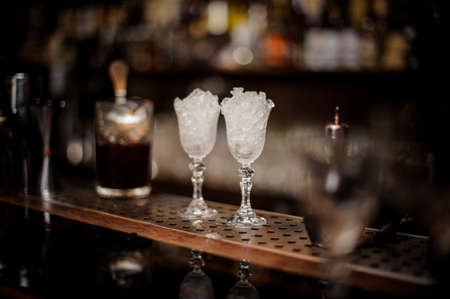 Two elegant cooled glasses filled with ice arranged on the bar counter against the blurred background of restaurantの写真素材
