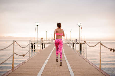 Back view of slim and young girl running over the wooden bridge during the beautiful sunriseの写真素材