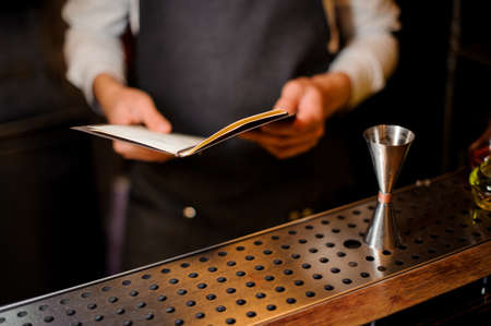 Bartender standing on the bar counter with a recipe book ready to preparing an alcoholic summer cocktailの写真素材