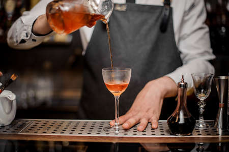 Professional bartender pourring a fresh alcoholic cocktail drink into the cocktail glass on the steel bar counterの写真素材