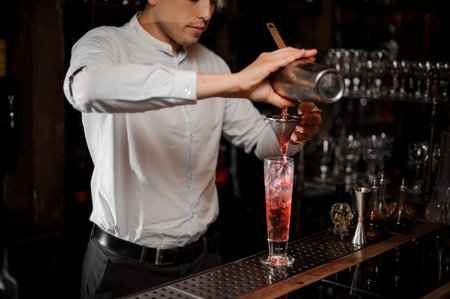 Barman pouring sweet and cold strawberry mojito summer cocktail into the glass on the bar counter
