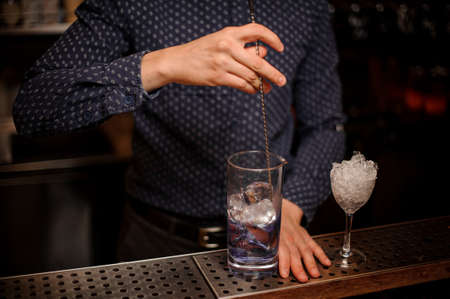 Barman stirring vodka with a blue syrup in a glass for making fresh and strong summer cocktailの写真素材