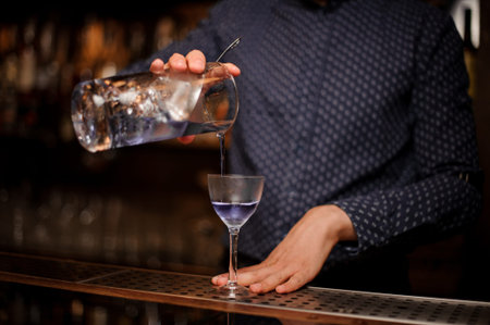 Barman pouring strong and fresh summer drink into the cocktail glass on the bar counter