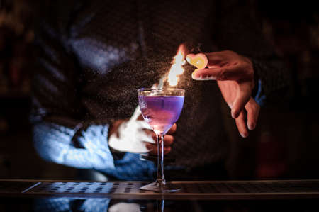 Bartender making a strong and fresh purple summer cocktail with a smoke note and orange juice on the dark backgroundの写真素材