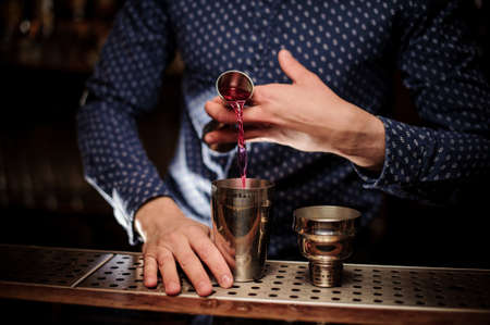 Bartender pouring a portion of pink alcohol drink into the shaker for making fresh summer cocktailの写真素材