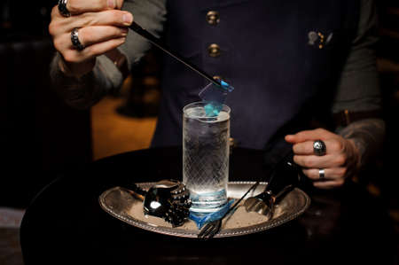 Professional bartender decorate a cocktail glass with a transparent blue caramel sheet on the silver trayの写真素材