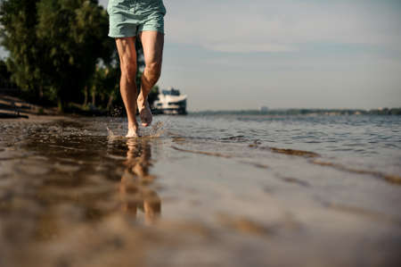 Muscular male feet running along the river bank on sunny summer day on the background of trees and skyの写真素材