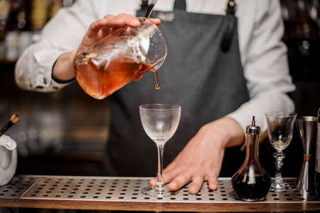 Bartender pouring fresh alcoholic drink into the cocktail glass making summer cocktail on the bar counterの写真素材