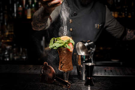 Bartender adding powder to a fresh summer cocktail with mint, orange and strawberries on the bar counter among the bartender equipmentの写真素材