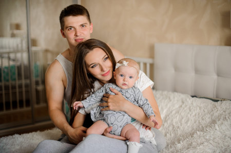 Father sitting behind mother and their little daughter on the bed in their cozy domestic room