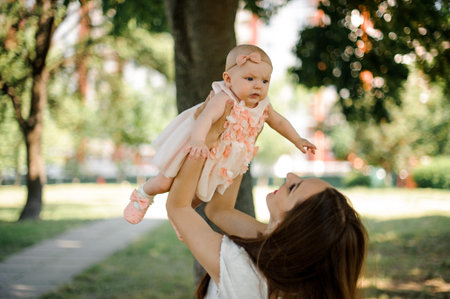 Mother holding her lovely little daughter in the white dress up in the air in the puclic green park