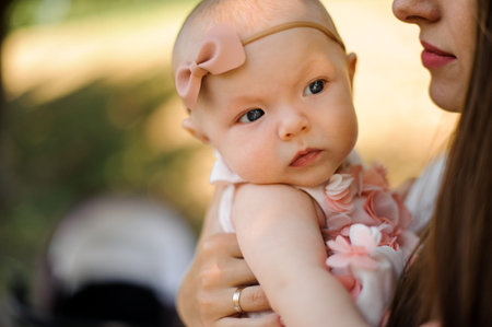 Young brunette mother holding her little blondie daughter on the hands in the public park on the...