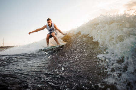 Strong and young wakesurfer riding down river waves against clear sky on hot summer dayの写真素材