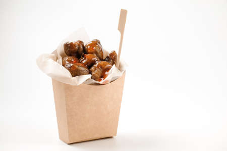 Isolated paper food bag filled with tasty chestnuts with teriyaki and sweet chilli sauce on bright white backgroundの写真素材