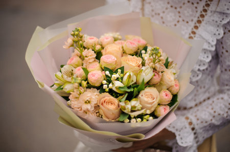 Girl holding in her hands a beautiful bouquet of champagne color pink roses in the gift paper in the...