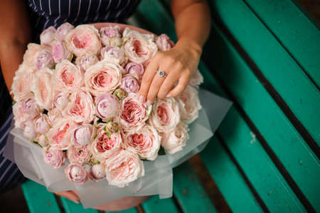 Girl in the blue dress holding in her hands a beautiful bouquet of pastel color rose peonies in the gift paper sitting on the benchの写真素材