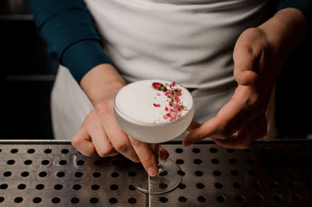 Bartender girl serving a white cocktail with scum decorated with dried flowers and silver colored beadsの写真素材