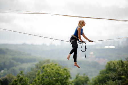 Side view young blondie woman sitting on the slackline rope on the background of houses among trees...