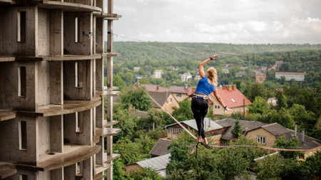 Rear view blondie girl walking on the slackline rope on the background of houses among trees and...