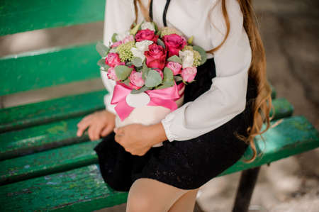 School girl sitting on a bench and holding a box with rosesの写真素材