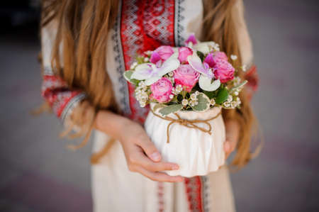 Woman in national ukrainian blouse embroidery holding a cute white pot of pink and red rosesの写真素材