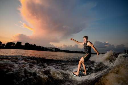 Active man riding on the wakesurf down the river on the background of beautiful sky