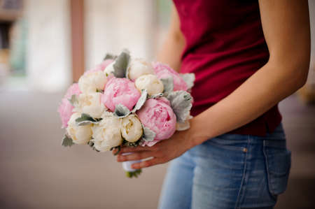 Girl in red shirt and jeans holding in her hands a beautiful bouquet of pink and champagne color tender peoniesの写真素材