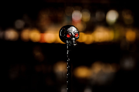 Black isolated skull-shaped spoon with red eyes on the blurred background of bar lights of club