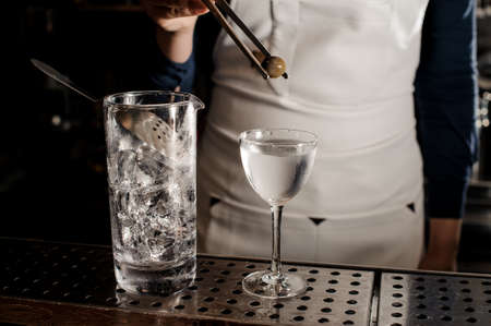 Barman putting a green olive into a fresh and tasty summer cocktail drink in a glassの写真素材