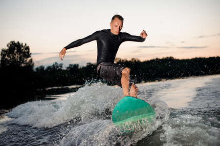 Wakesurfer in black swimsuit jumping on a wake board riding down the river at the eveningの写真素材