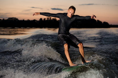 Active wakesurfer in black swimsuit jumping on a wake board riding down the river at the summer...