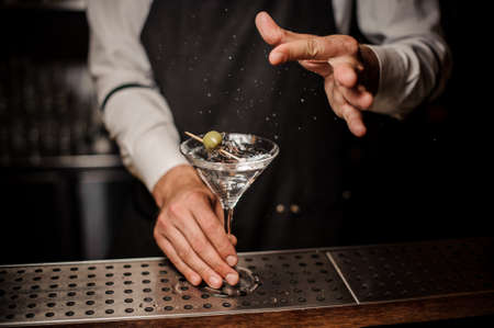 Barman making a fresh and strong martini summer cocktail with a green olive and saltの写真素材