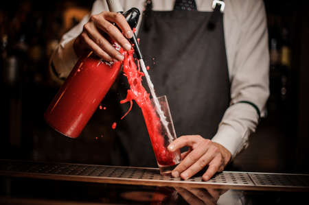 Barman pouring alcoholic sparkling water into a sweet red berry summer cocktail on the bar counterの写真素材