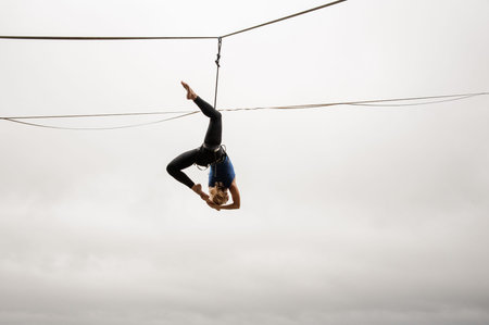 Brave blonde girl balancing high on a slackline against the grey sky on rainy summer day