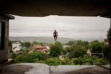 Athletic man keeping balance on a slackline against the sky and trees on rainy summer dayの写真素材