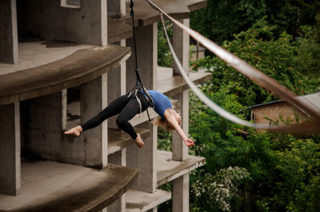 Brave blonde woman balancing and hanging in air on the background of empty building and trees