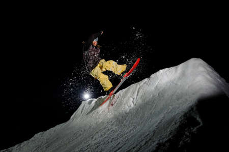 Freeride snowboarder with dreadlocks dressed in the yellow sportswear is jumping in in the mountains at nightの写真素材